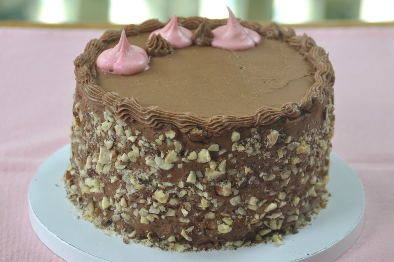 Rich chocolate cake topped with hazelnut buttercream frosting and decorated with toasted hazelnuts.